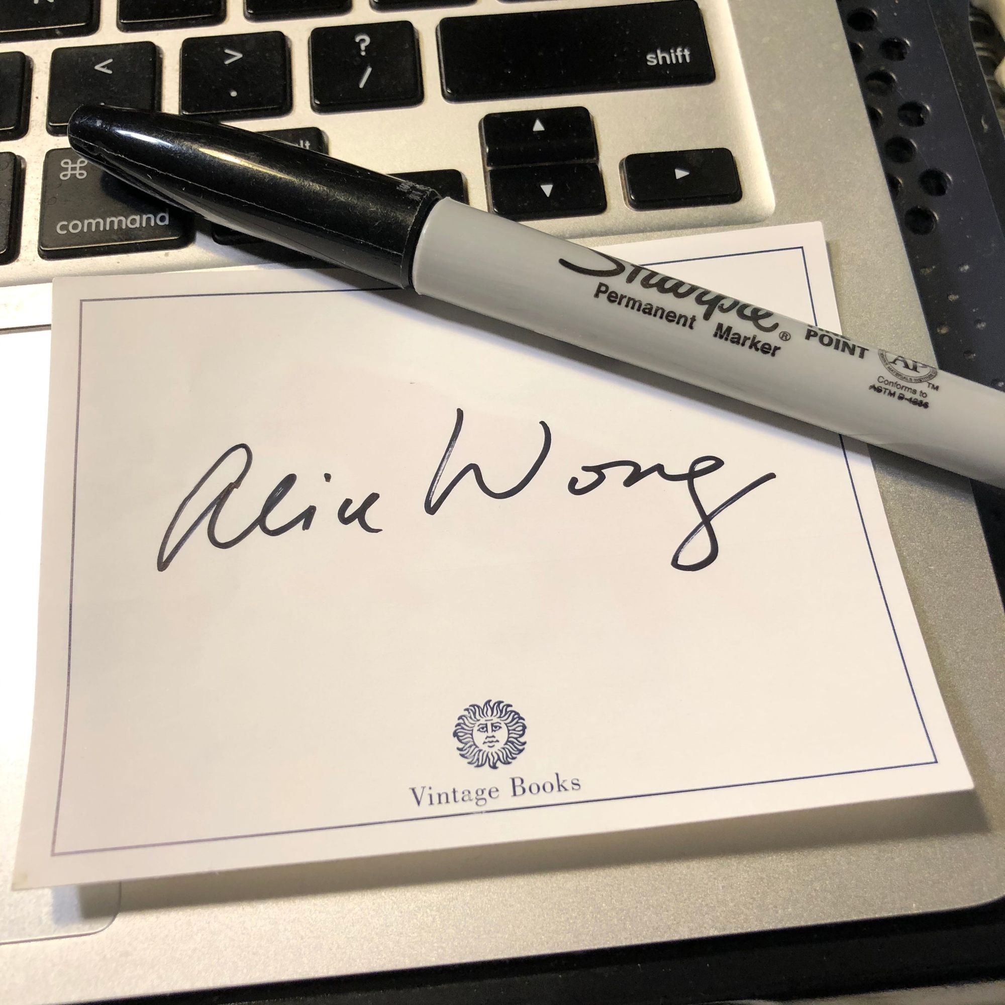 Photo of a cream-colored bookplate by Vintage Books with a signature by Alice Wong resting on top of a laptop with a black Sharpie pen above at a slight diagonal. 