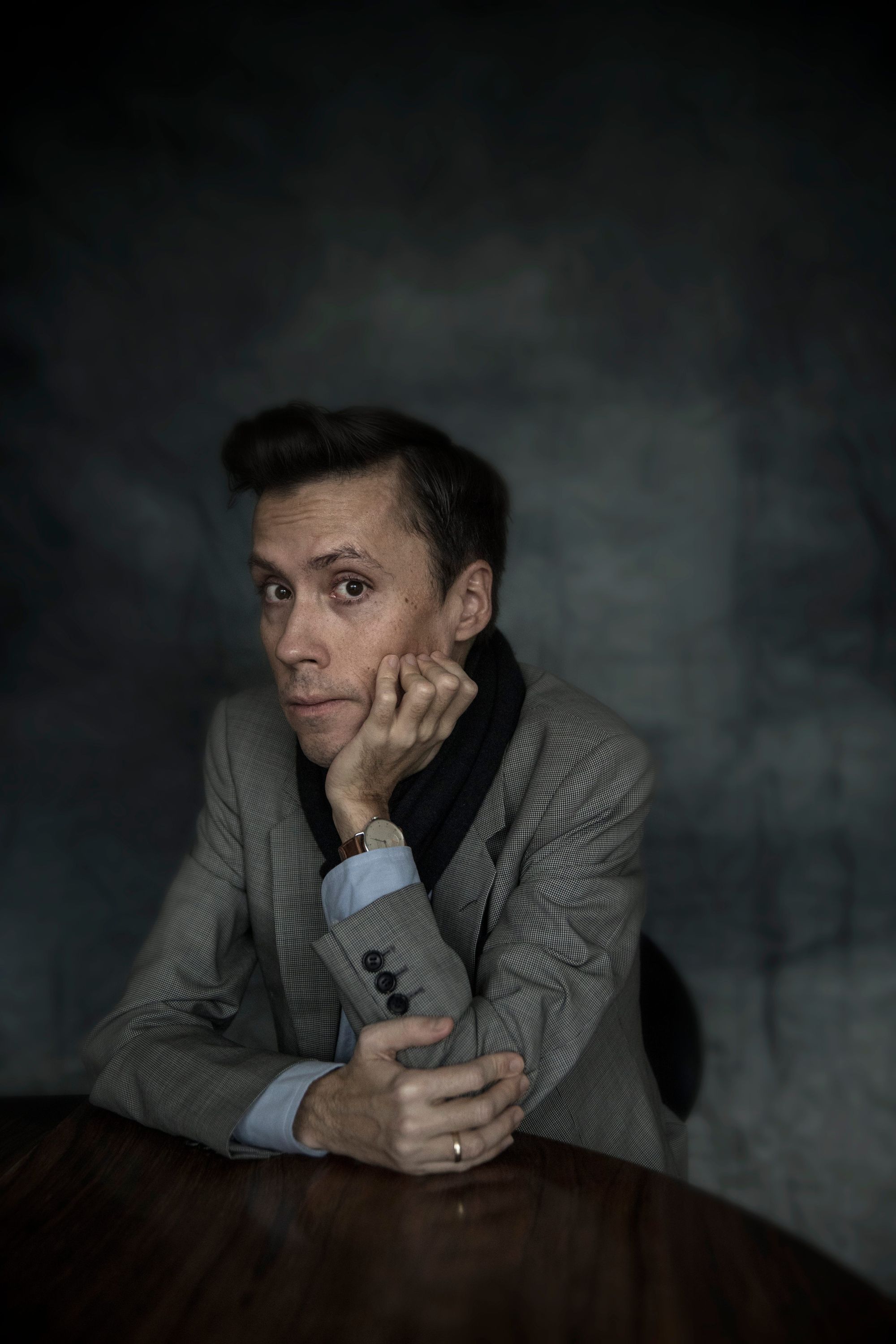 The author, Jan Grue, is seen from the torso up, wearing a suit and looking at the camera from behind a table. His left elbow is propped on the table, with his left hand resting under his chin and watch on his wrist. His right arm is resting flat on the table, with his right hand clasping his left elbow and a wedding ring on his finger.