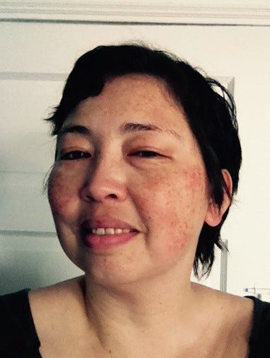 A headshot of author Claire Light (writing as Jadie Jang) smiling at the camera, with her face slightly angled to the side and in front of a closed white door.